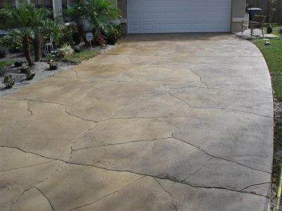 Cracked concrete driveway leading to a closed garage, with landscaping along the left side.