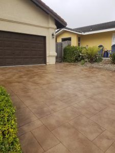 Wet tiled driveway beside a beige house with a dark garage door and small shrubbery