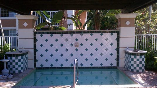 Small tiled pool or hot tub under a patio, with blue diamond wall tiles and metal handrails.