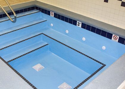 Empty indoor pool with blue water and tiled walls, viewed from the corner.