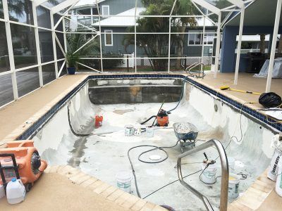 Drained backyard pool under a screened enclosure, with construction tools and repainting in progress