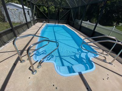 Accessible pool with a metal handrail and bright blue water under a screened enclosure