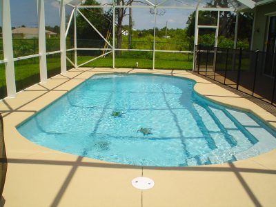Small backyard swimming pool with blue water and screened patio enclosure under bright sunlight
