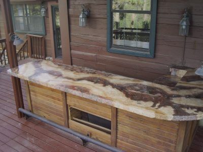 Weathered outdoor wooden cabinet on a porch with a mottled white and brown countertop, beside a house wall and windows