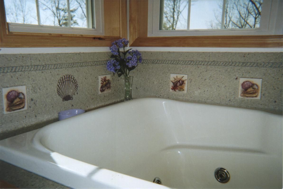 White bathtub beneath windows with floral tile decor and a vase of purple flowers on the ledge