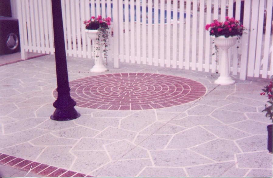Patio with patterned stone floor, round brick inlay, white fence, flower urns, and a black lamp post
