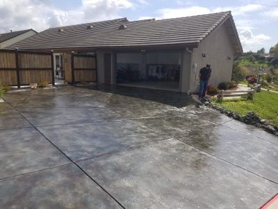 Large wet concrete driveway beside a single-story house, with one person standing near the garage.