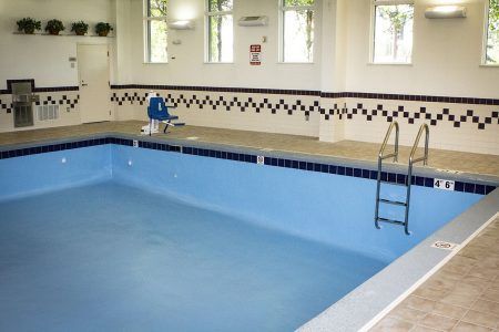 Indoor swimming pool with blue water, tiled deck, ladder, and safety railings.