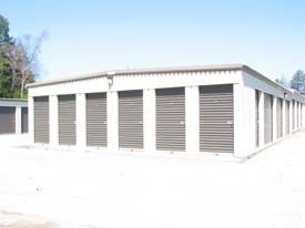 A row of storage units with brown doors in a parking lot.