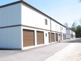 A row of white buildings with brown garage doors on a sunny day.