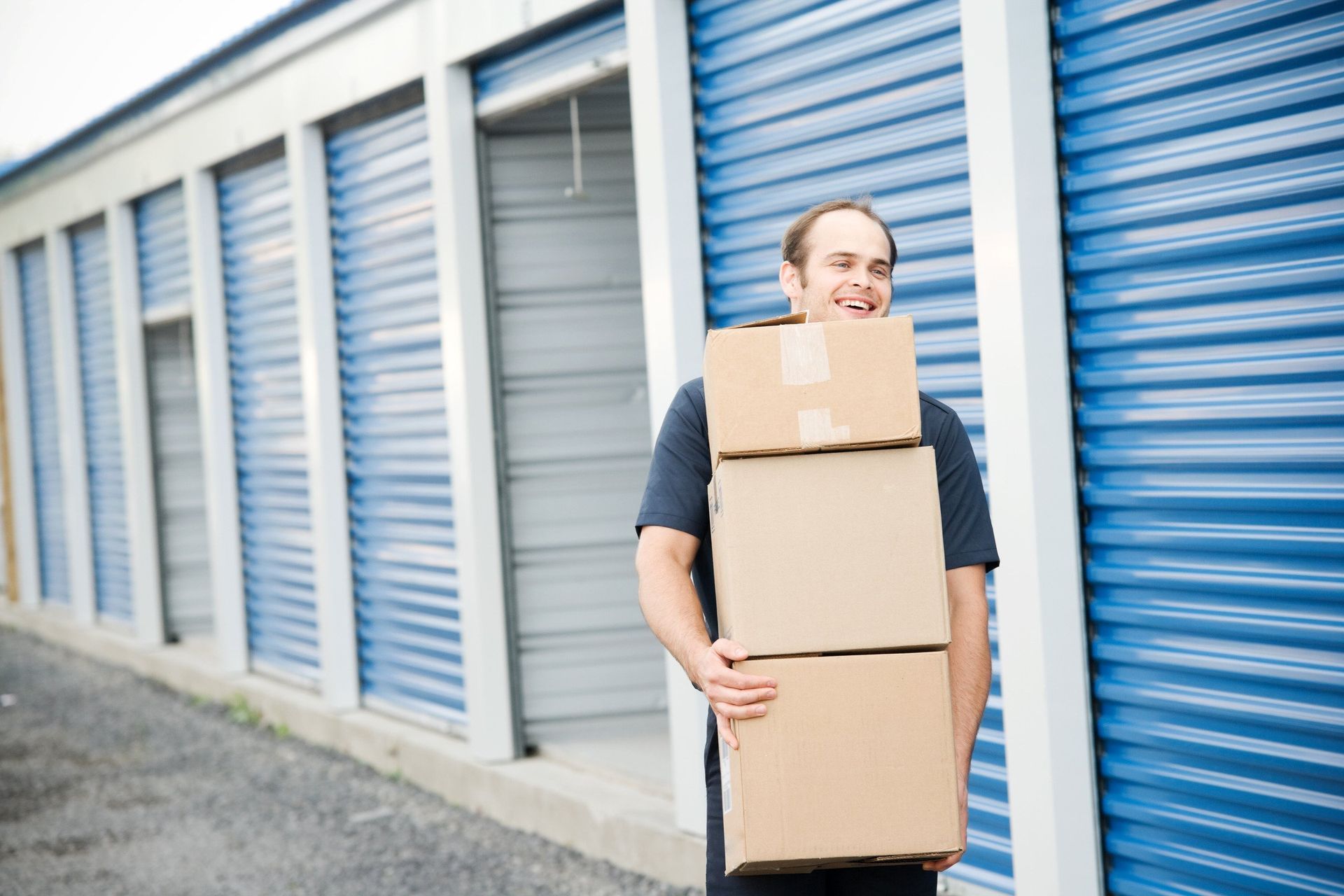 A man is holding a stack of cardboard boxes in front of a storage unit.
