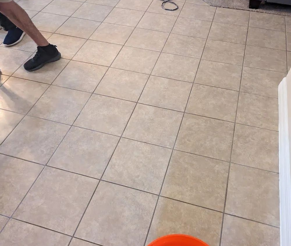 Tiled floor with part of a person’s leg and shoe at left, and a bright orange object at bottom edge