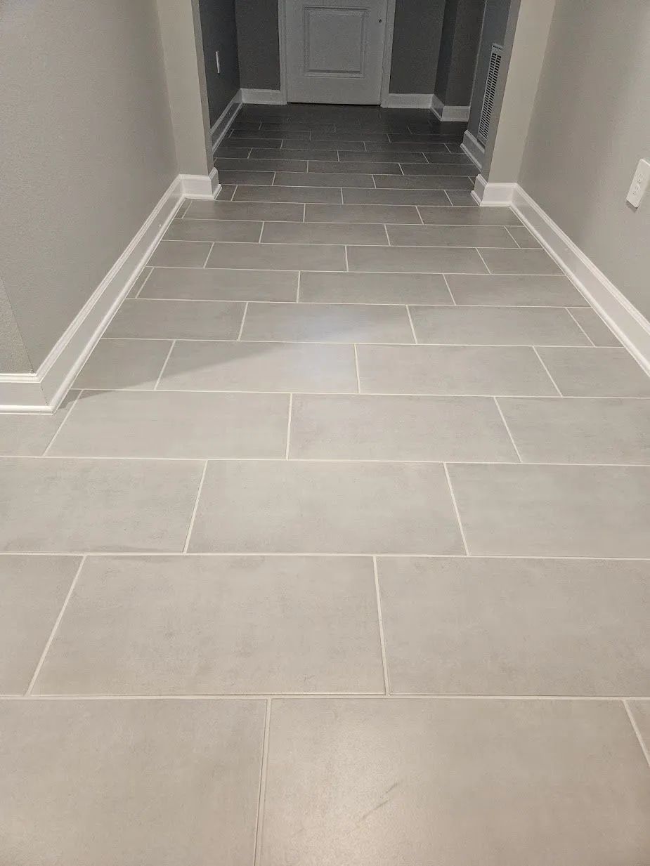 Empty gray-tiled hallway with white baseboards and doors at the far end