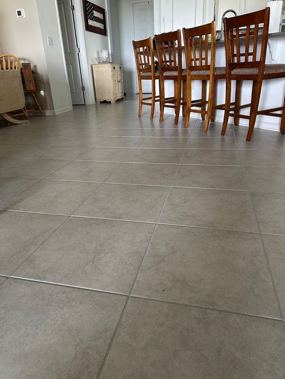 A row of wooden chairs are lined up on a tiled floor in a kitchen.