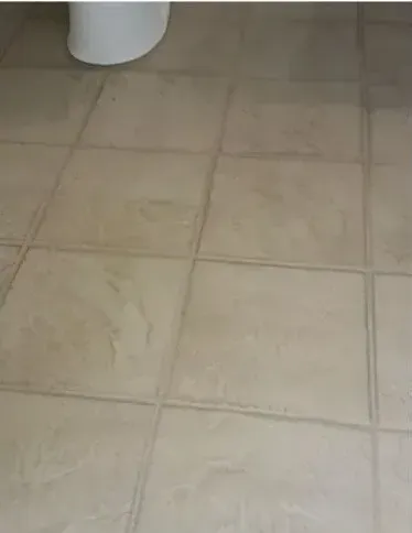 A close up of a tiled floor with a toilet in the background.