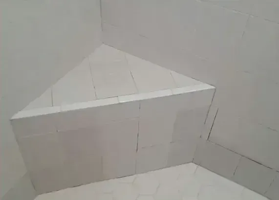 A bathroom with white tiles and a corner shower seat.