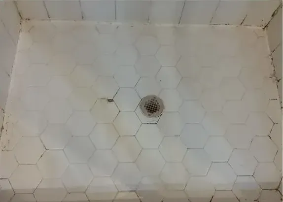 A shower stall with white tiles and a drain.