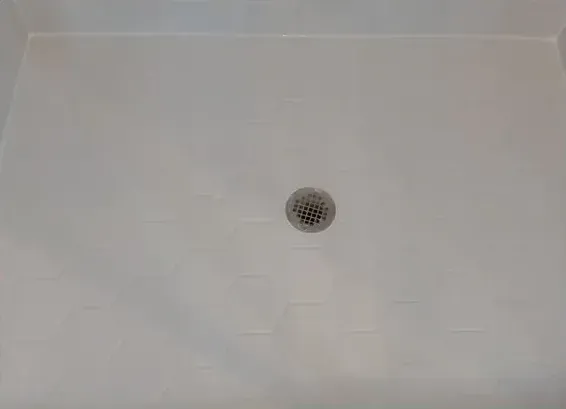 A white shower stall with a drain on the floor.