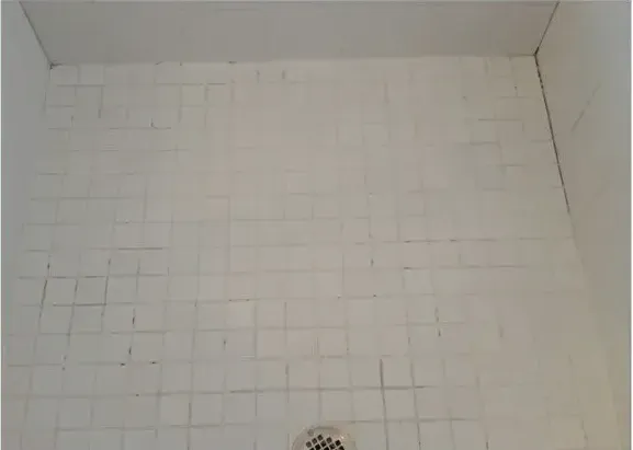 A white tiled floor in a bathroom with a drain.