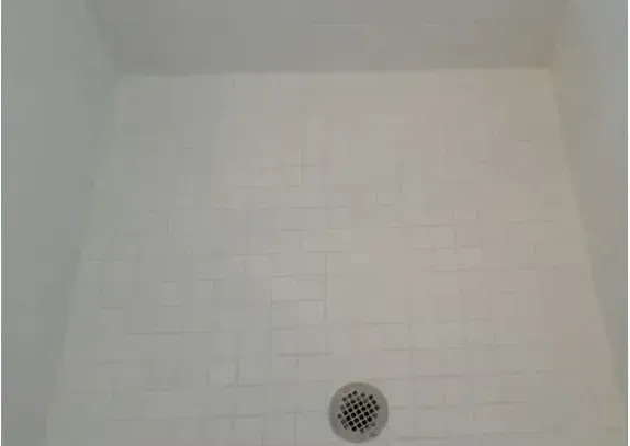 A white shower stall with a drain on the floor.