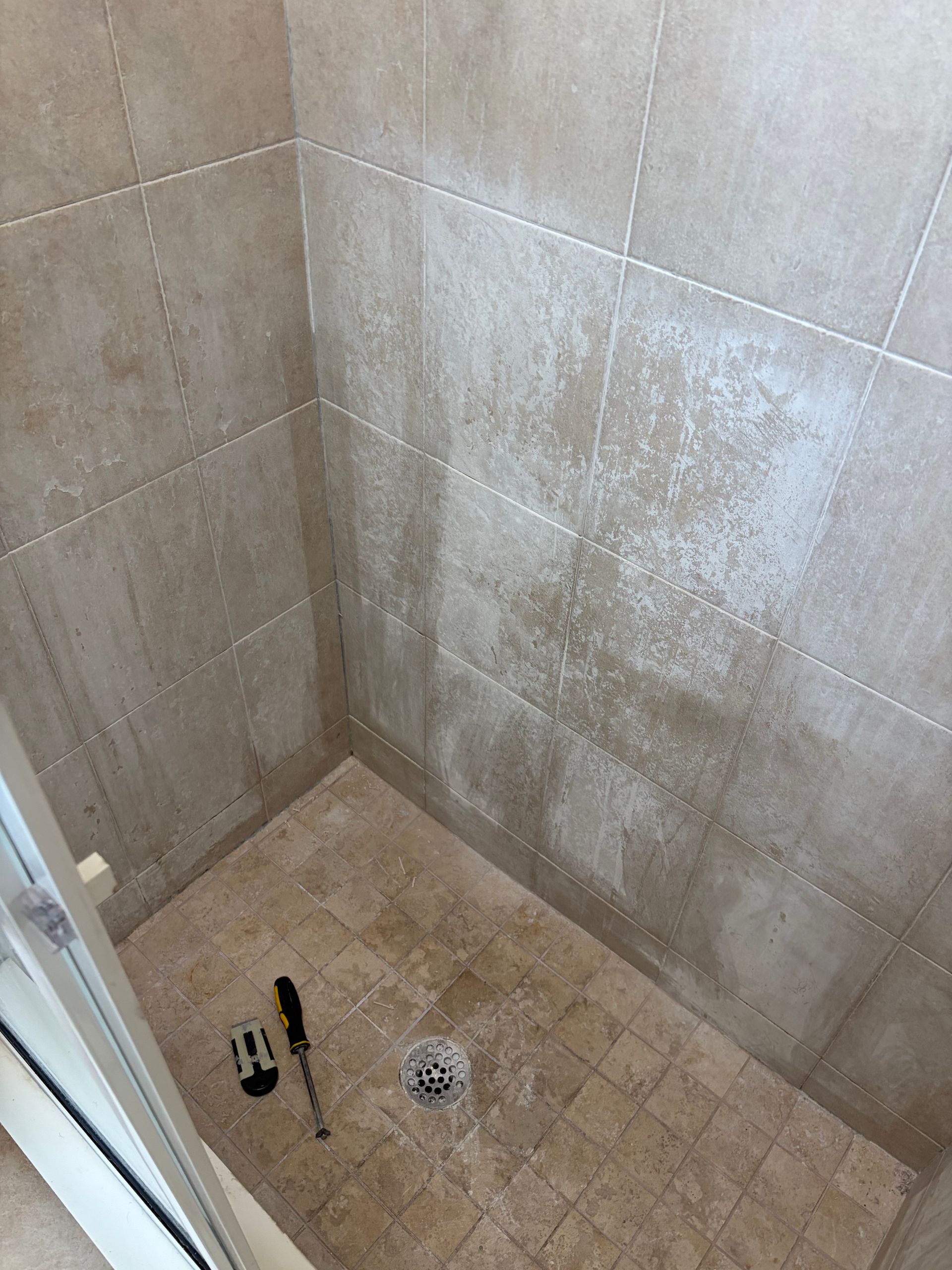 A shower stall with a glass door and white tiles in a bathroom.