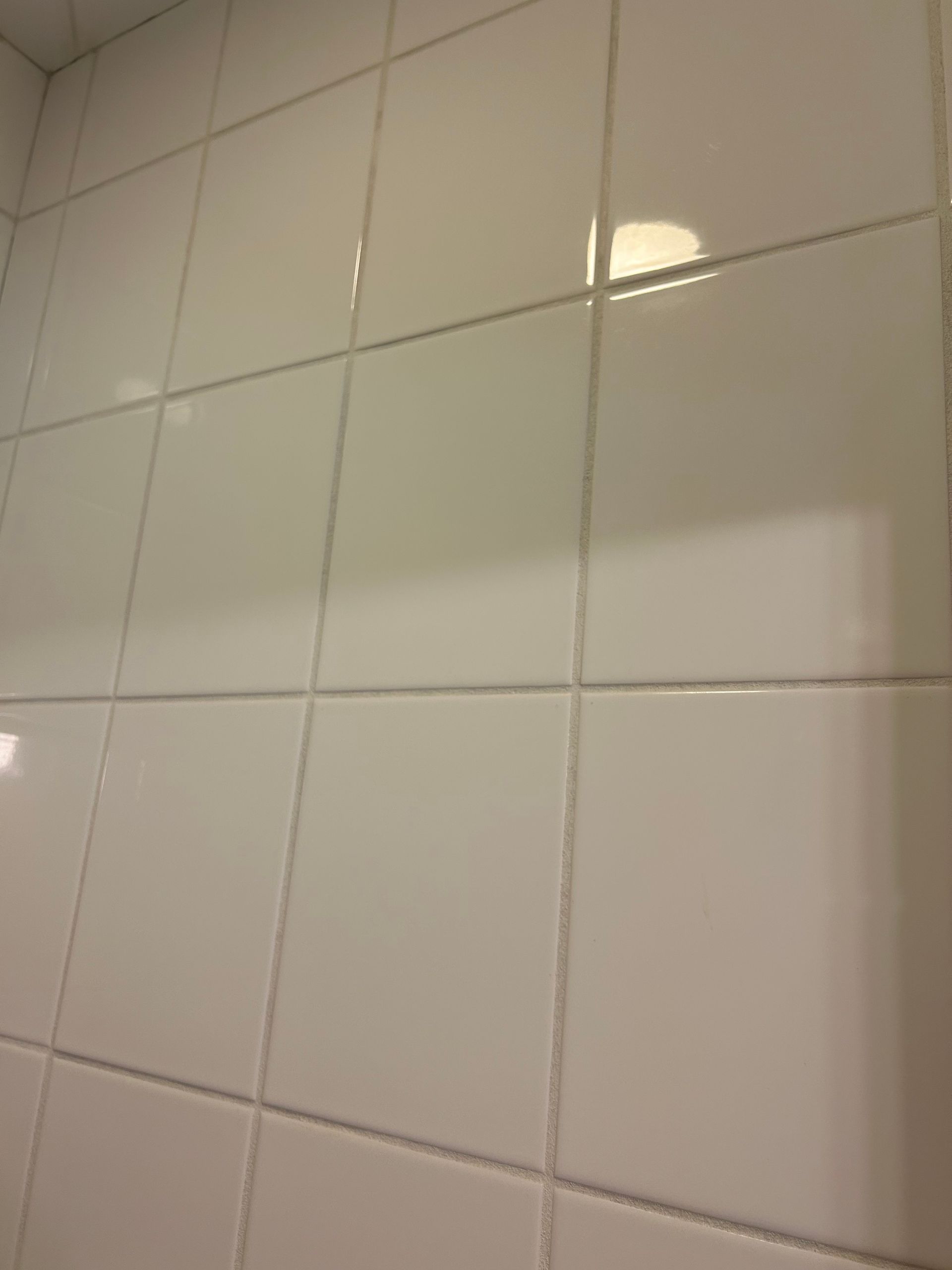 A shower stall with white tiles and a drain.