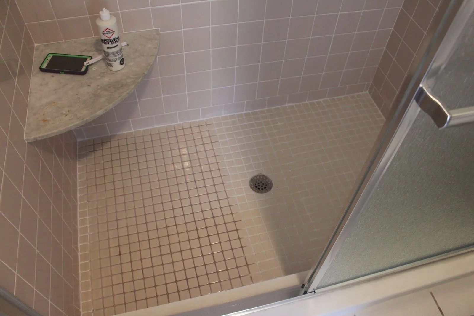 Shower with pink tiles, corner shelf, and glass door.