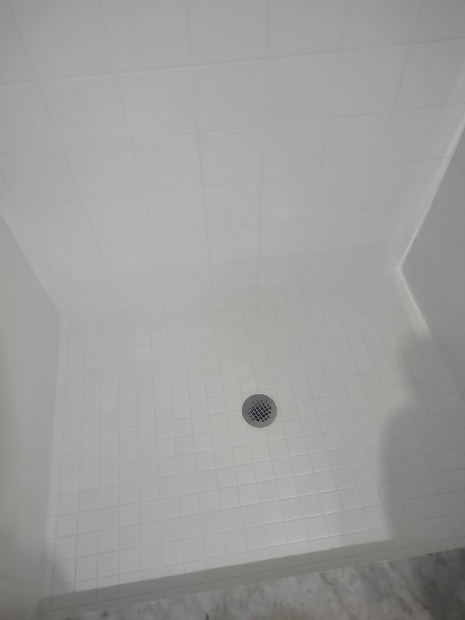 A shower stall with white tiles and a drain in a bathroom.