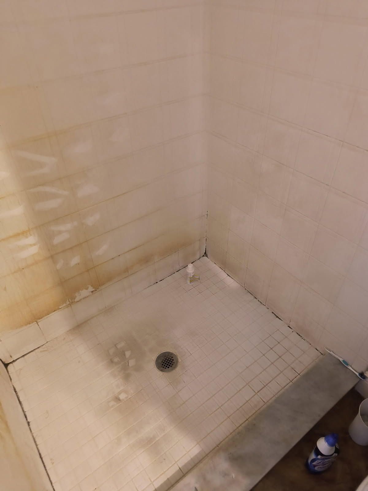 A dirty shower stall in a bathroom next to a toilet.