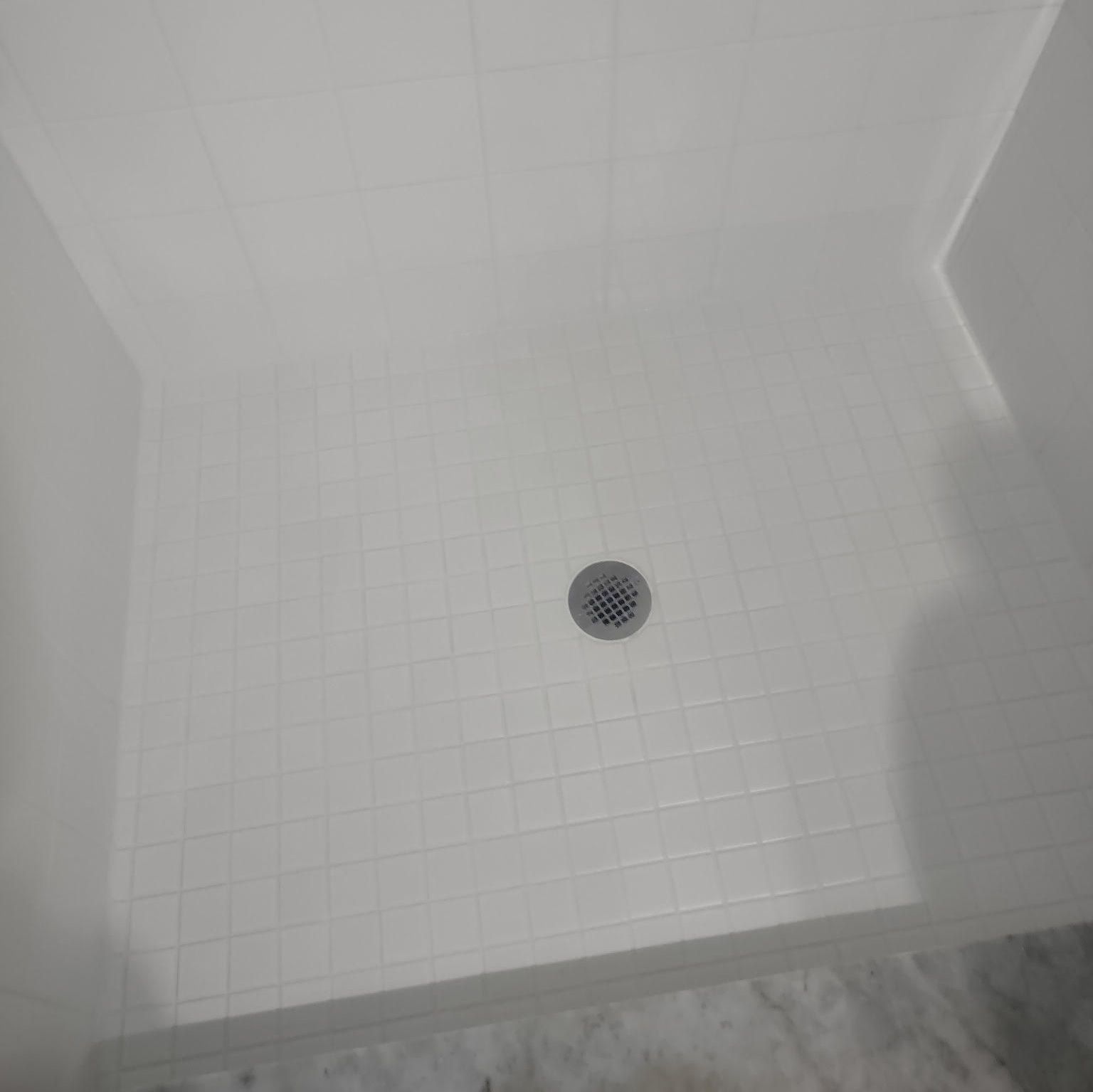 A shower stall with white tiles and a drain.