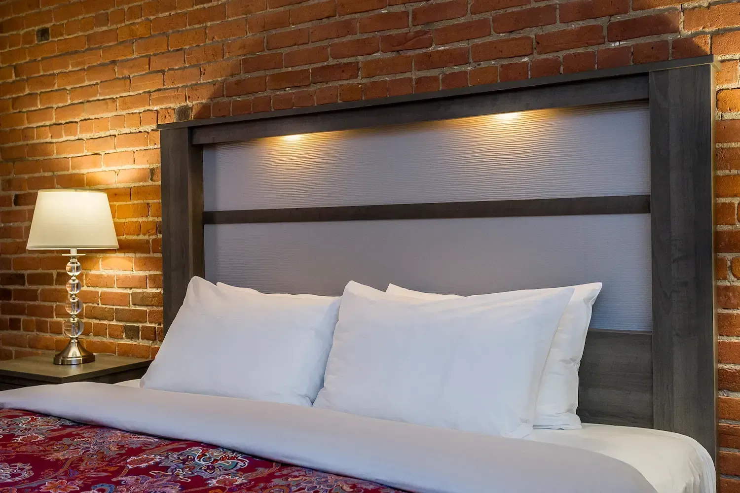 Un lit avec des draps blancs et des oreillers dans une chambre d'hôtel avec un mur de briques.