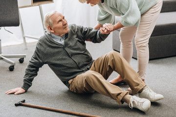 A woman is helping an elderly man who has fallen.