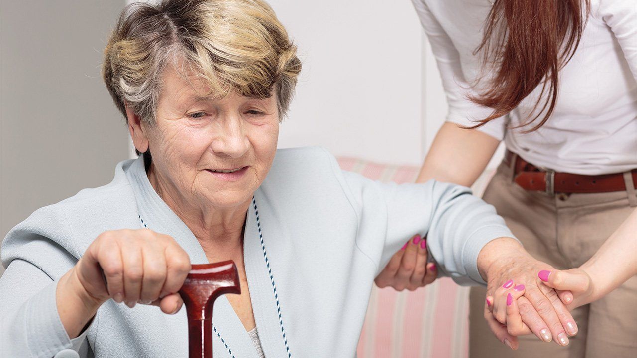 A woman is helping an elderly woman with a cane.