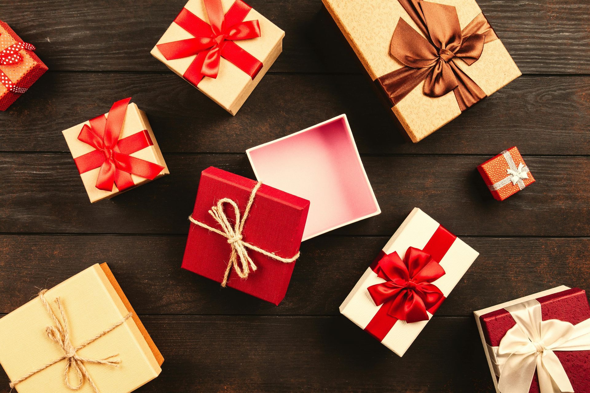 Gift boxes with red and brown bows on a dark wood surface. One box is open.