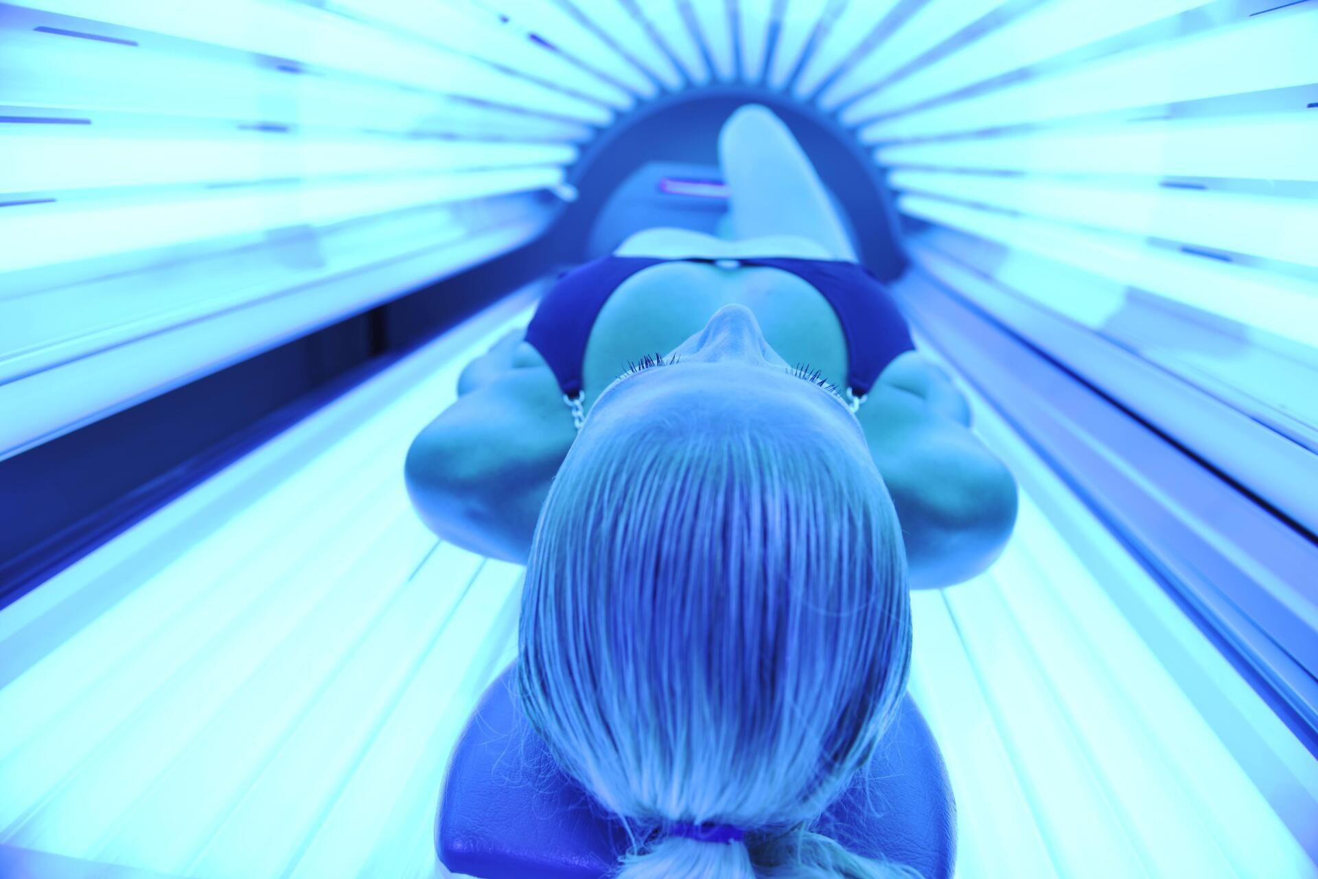 Person laying in tanning bed, blue light reflecting on body and face.