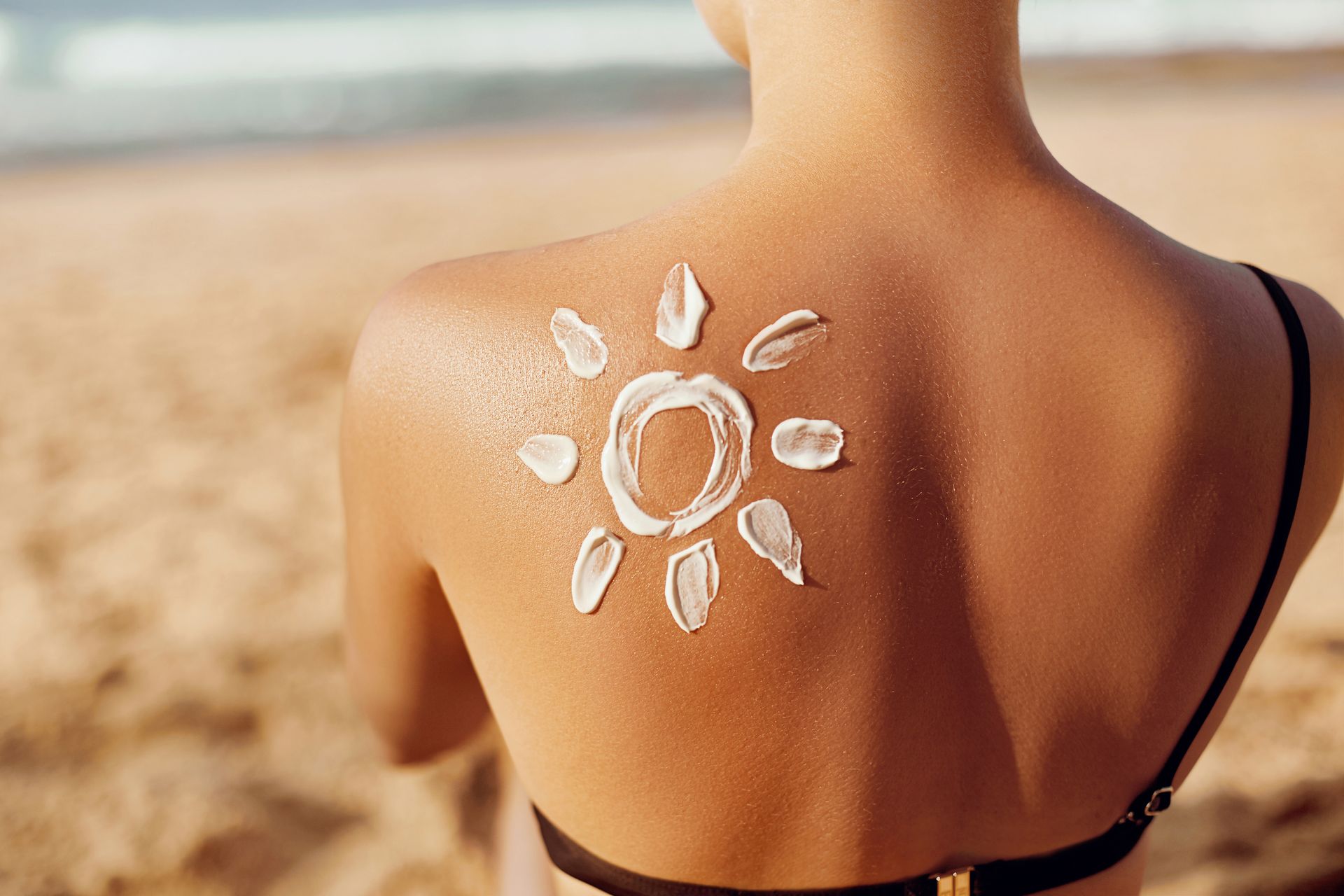 Person at beach with sunscreen shaped like a sun on their back.