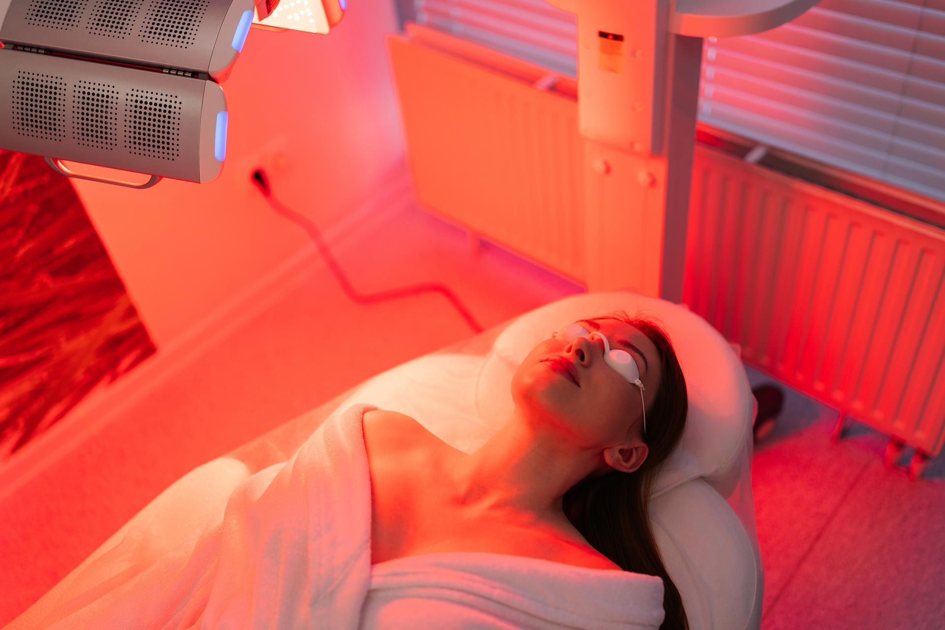 Professional red light therapy panel treatment for a relaxed woman wearing protective eye goggles.