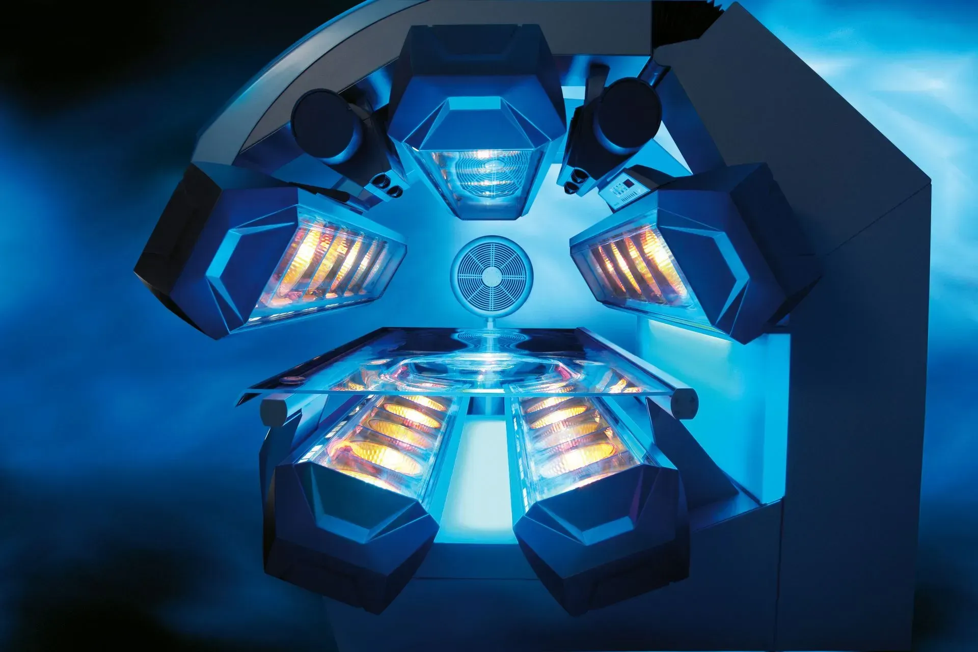 Blue tanning bed with six enclosed lamp sections, a central platform, and glowing light.