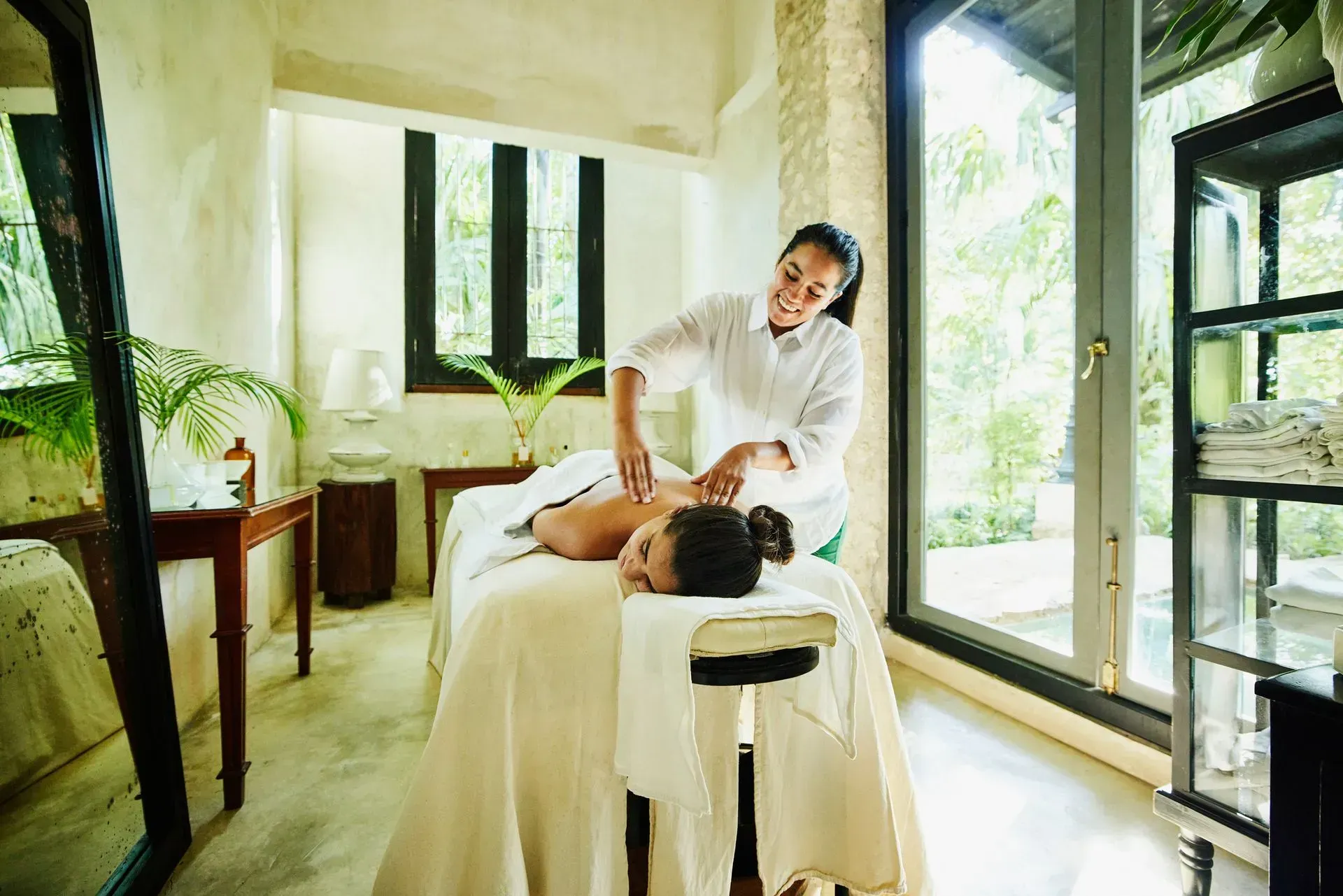 Woman receiving massage in a bright spa room; therapist applying pressure to back. Woman receiving massage in a bright spa room; therapist applying pressure to back.