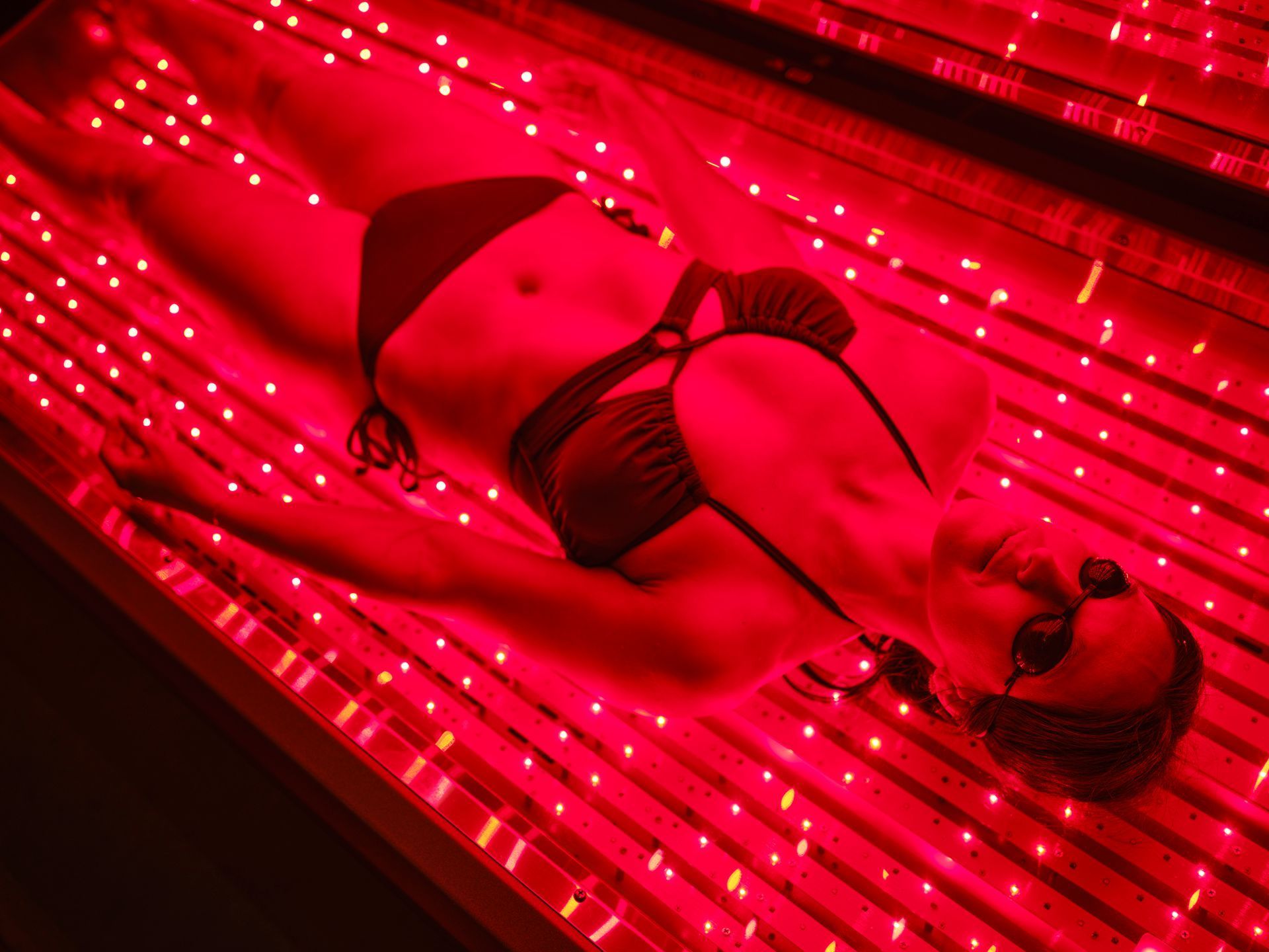 Woman wearing sunglasses in red light therapy bed.