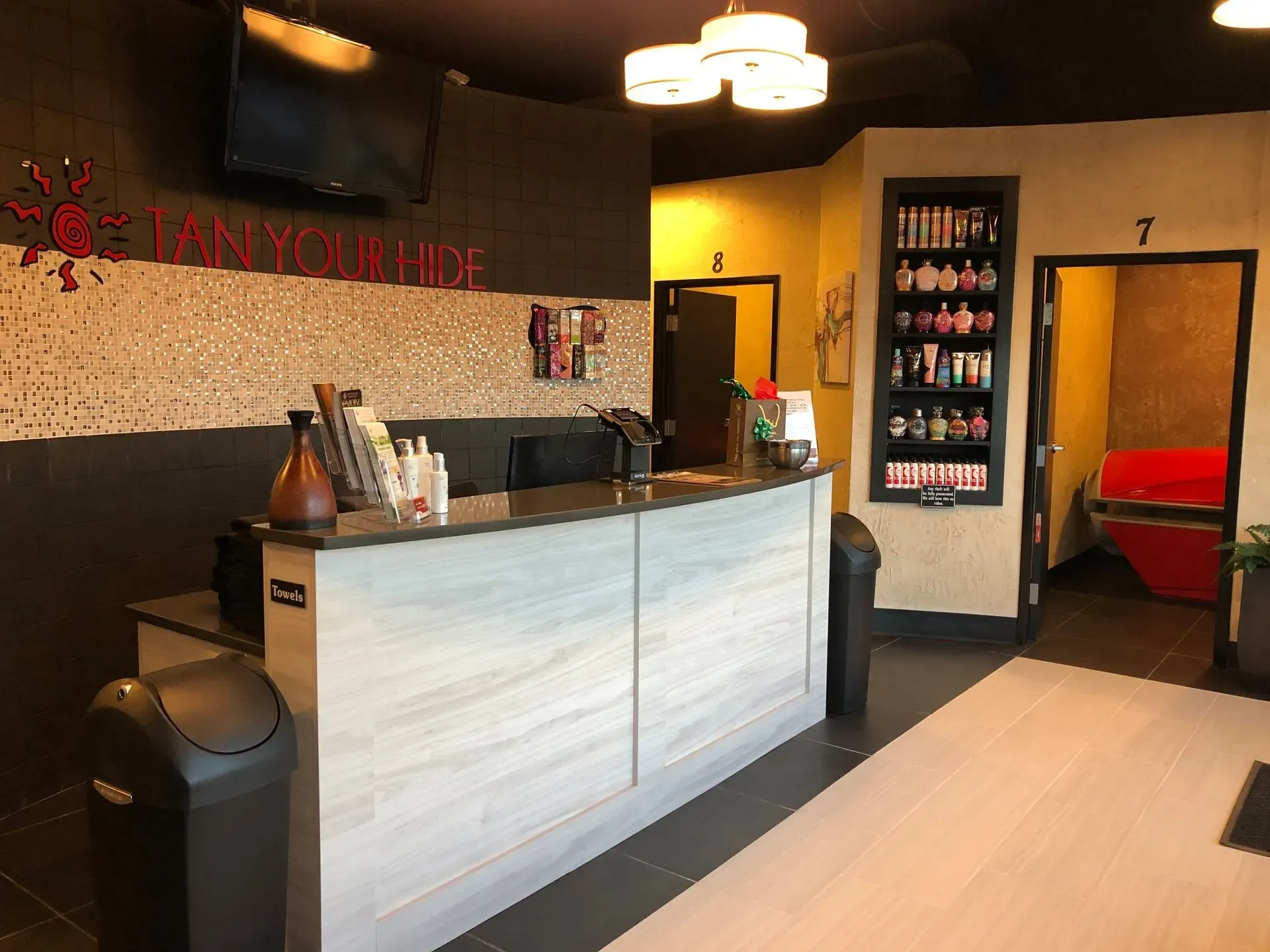 Tanning salon reception area with front desk, products, doorways, and a red tanning bed visible.