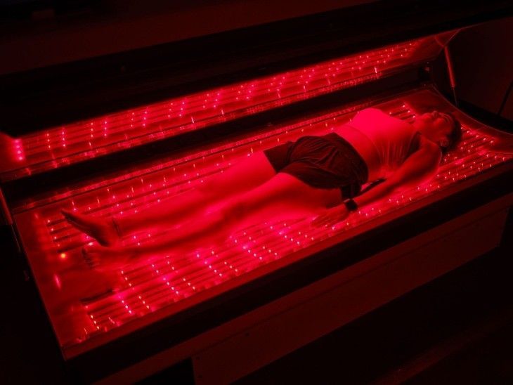 “Woman lying inside a red light therapy bed emitting rows of red LED lights”
