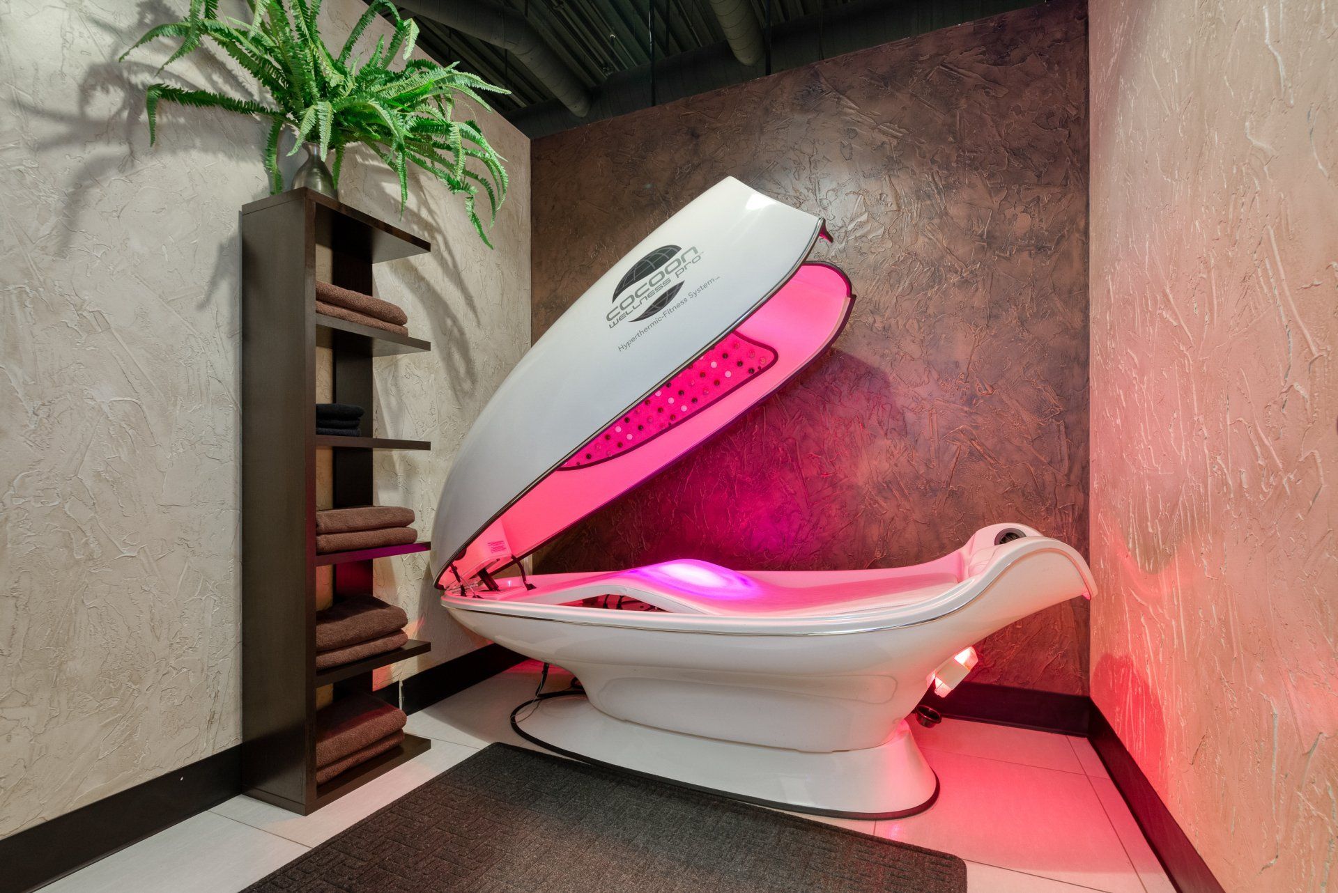 A white spa capsule with interior red light, open against a textured wall in a spa setting.