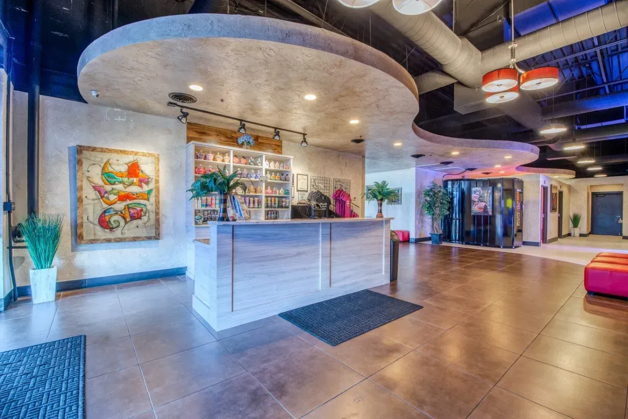 Lobby with a reception desk, art, plants, and curved ceiling. Wooden floor and accent lighting.
