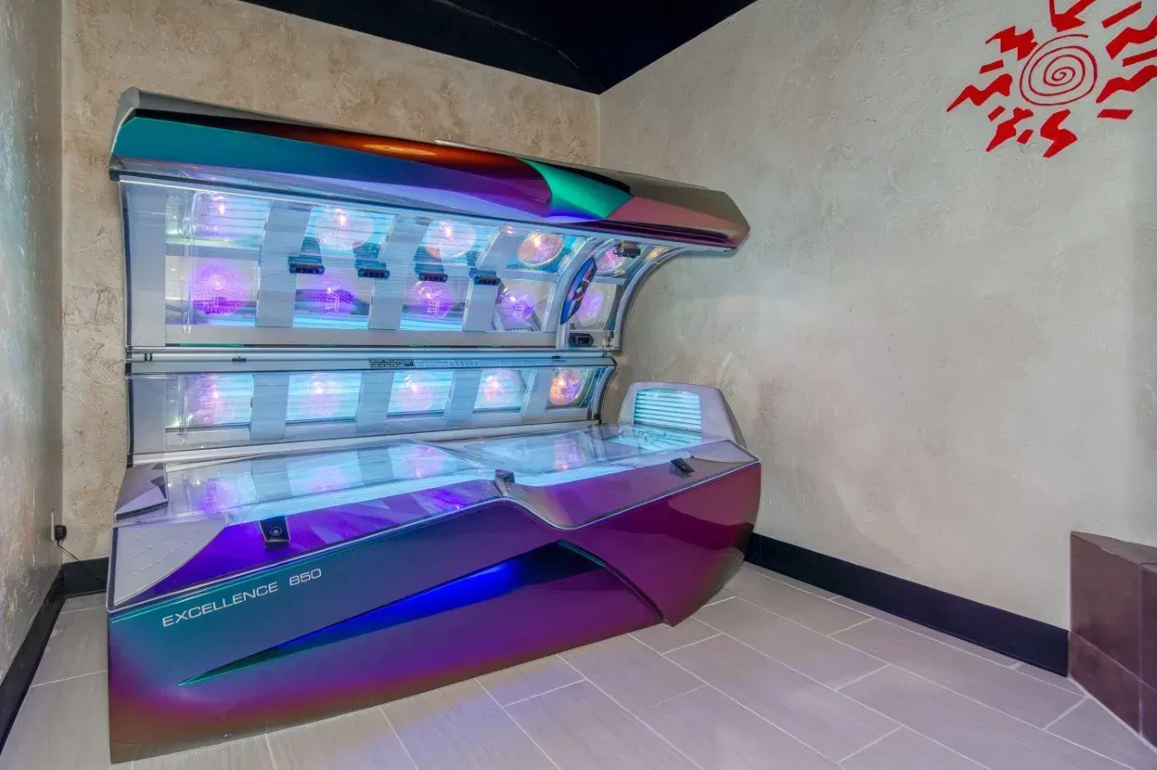 Tanning bed in a room with a sun-themed wall decoration and tiled floor.