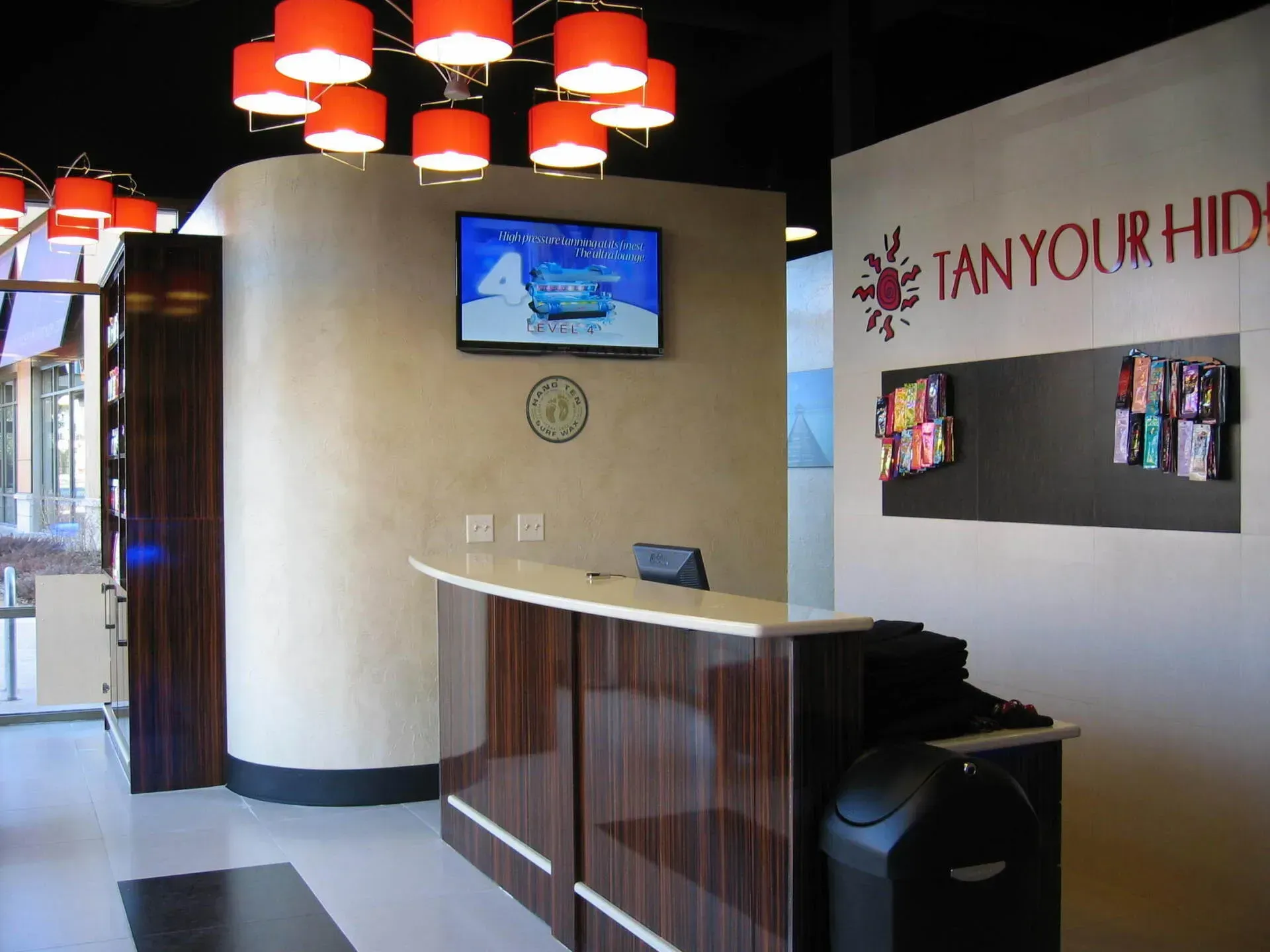 Reception area of a tanning salon with a dark wooden counter, a TV, and a sign that says 