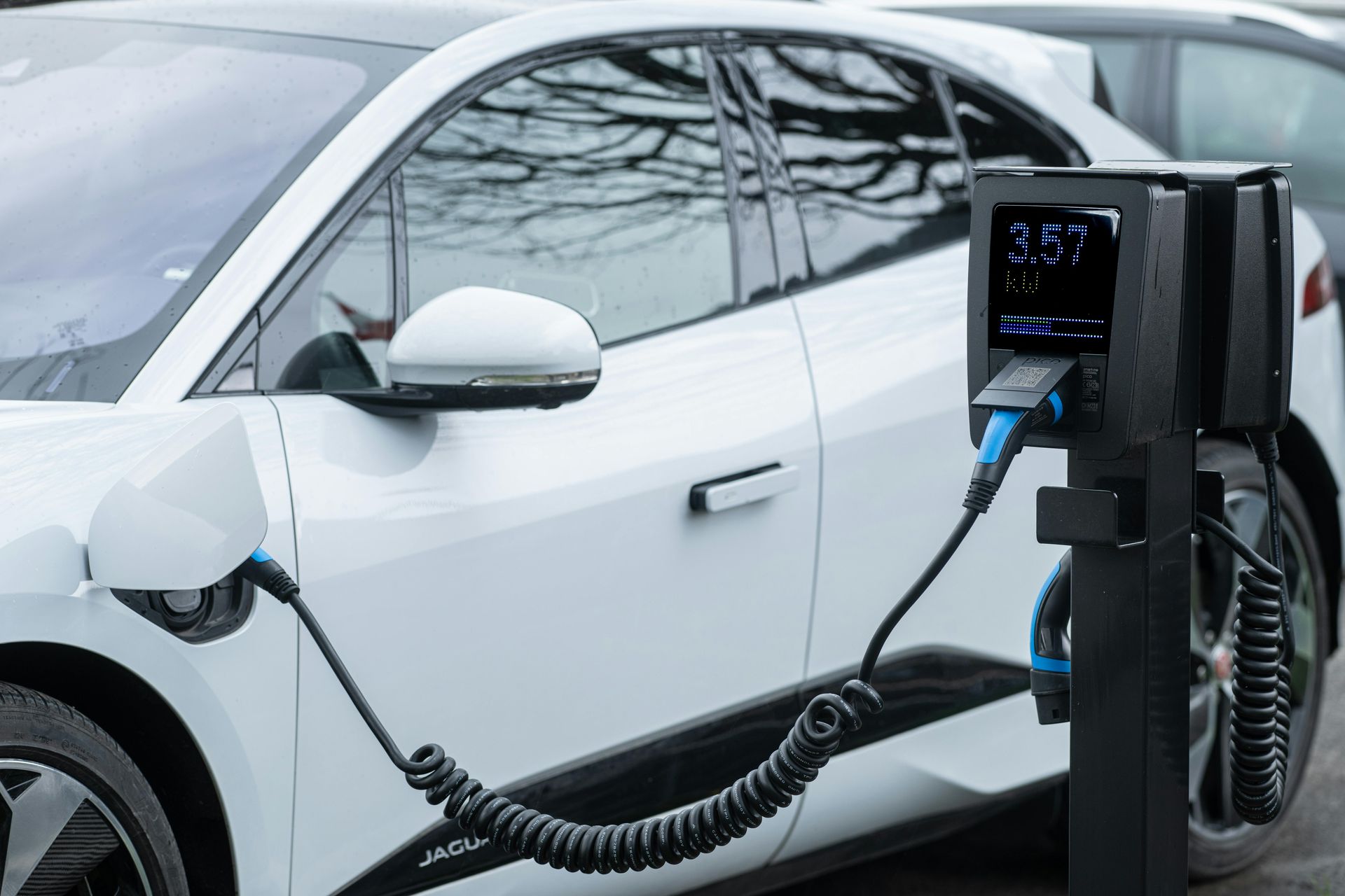 A white electric car is plugged into a black charging station outdoors.