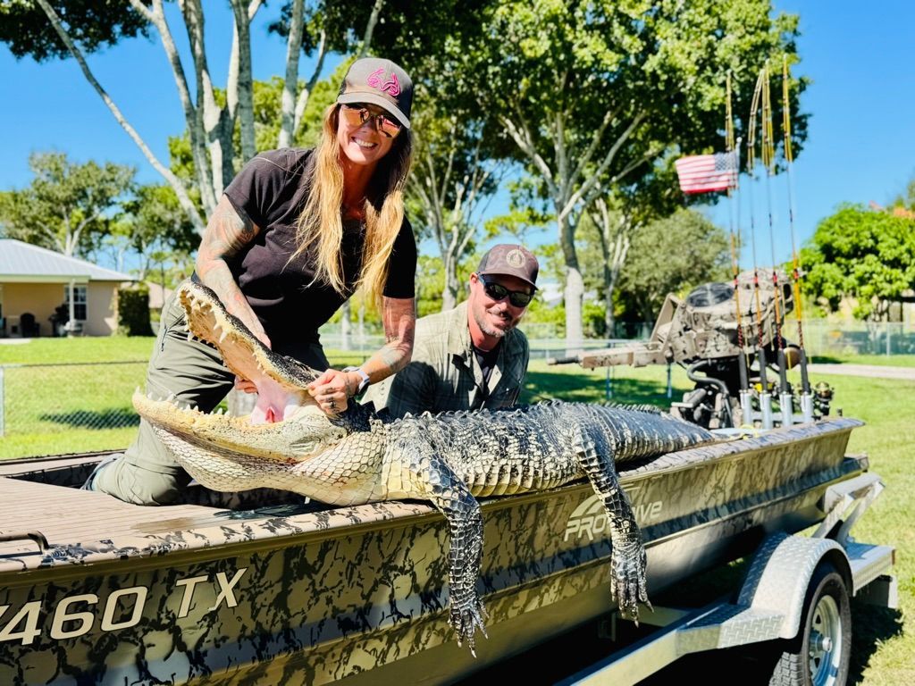 Two people kneeling beside a large harvested alligator on the bow of a mud boat, American flag in the background