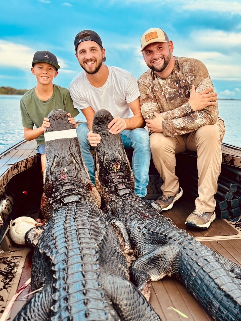 Three people including a young boy on a dark mud boat with two large harvested alligators