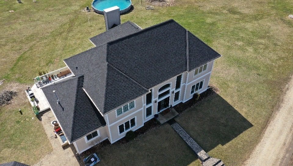 Aerial view of a white two-story house with a dark roof and a backyard pool on a grassy lot